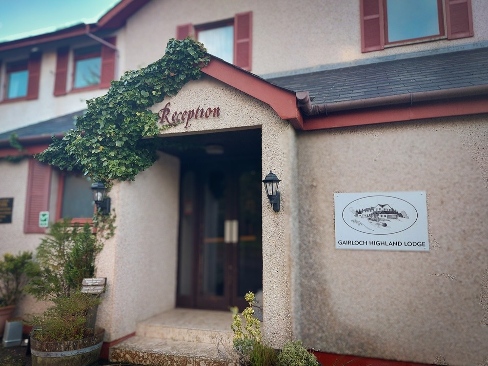 The entrance to Gairloch Highland Lodge reception, featuring the hotel sign and ivy-covered stone architecture in Gairloch.