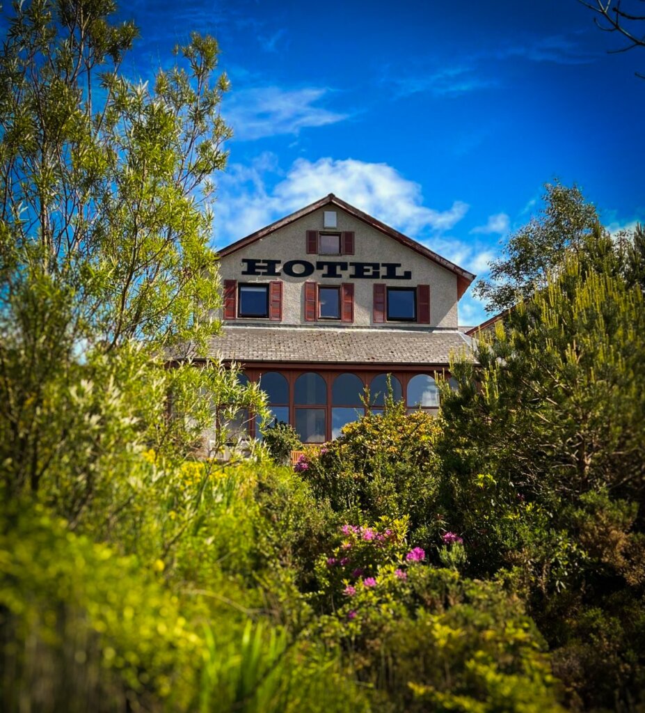 Exterior view of Gairloch Highland Lodge surrounded by lush greenery and flowers, a perfect stop for NC500 travellers.