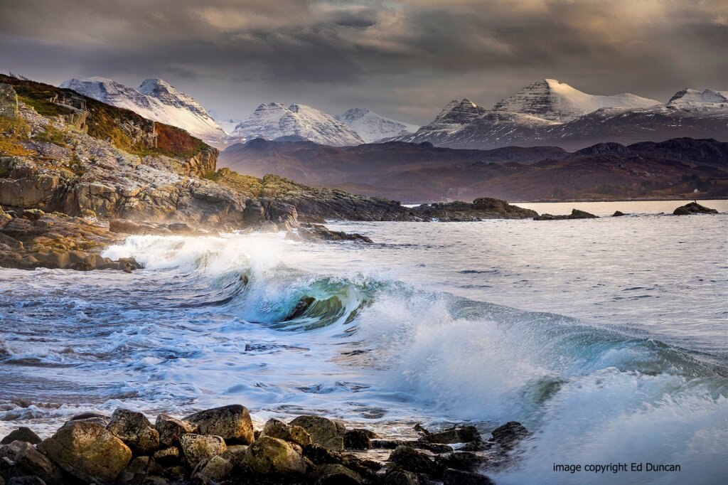 Waves crashing at Big Sand Beach with snow-capped Torridon Mountains in the distance, a top thing to do in Gairloch.